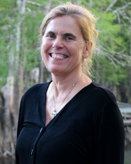 Julie Steward standing outside near trees in a black v-neck shirt smiling